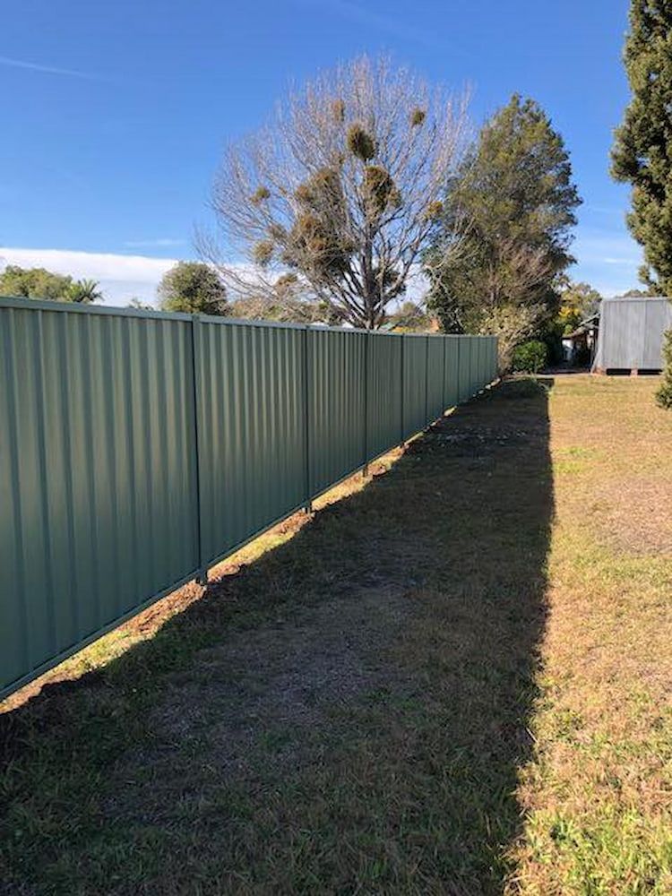 Green Corrugated Metal Fence Along a Grassy Yard With a Tree — Alcando Renovations and Maintenance In Bobin, NSW