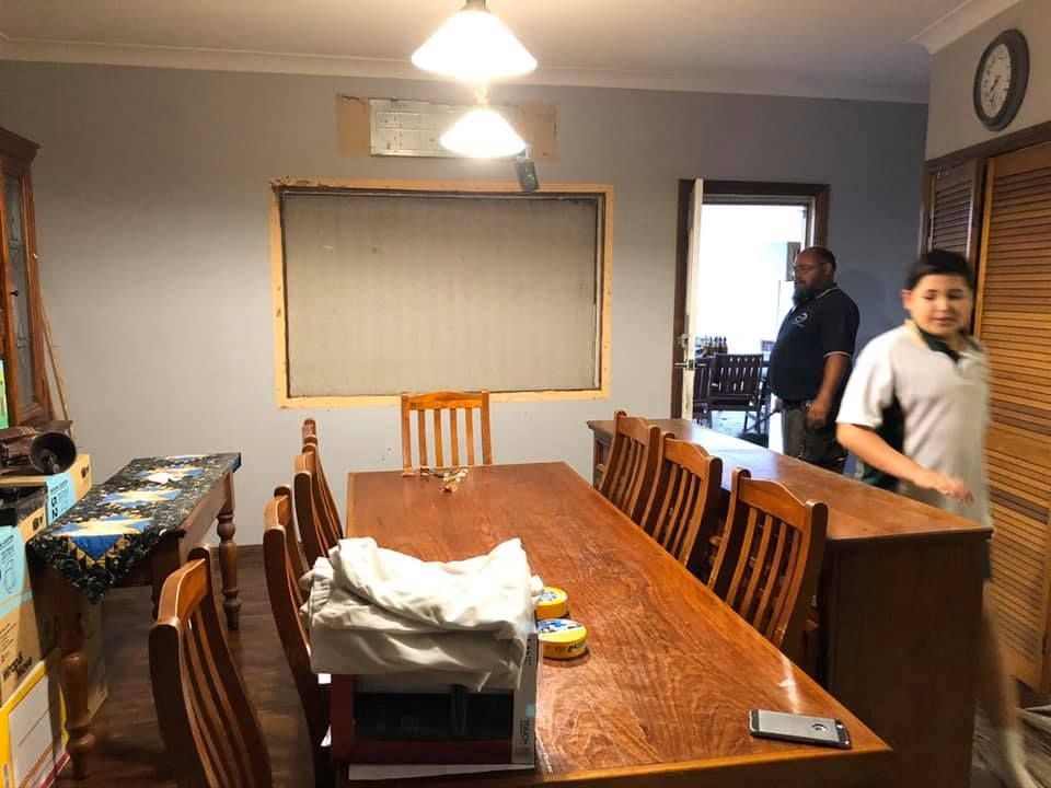 Dining Room With Long Wooden Table, Chairs, and Two People — Alcando Renovations and Maintenance In Bobin, NSW