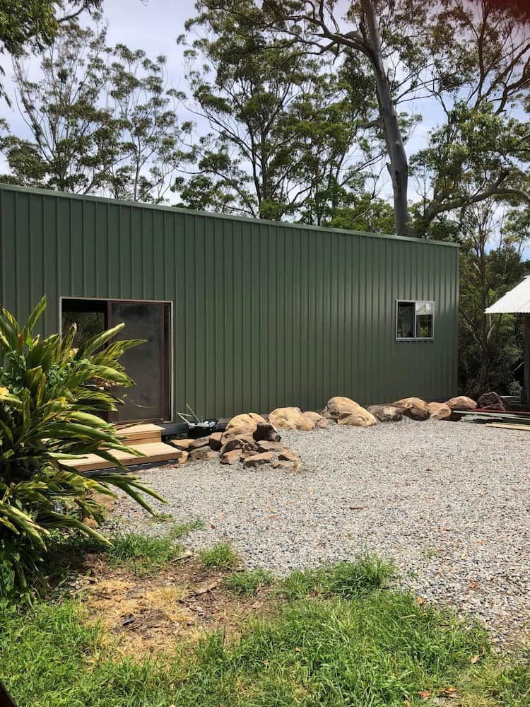 Green Corrugated Metal Building With a Gravel Driveway, Rocks, and Trees — Alcando Renovations and Maintenance in Bobin, NSW