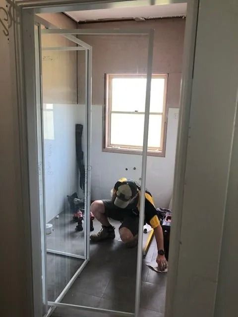 Person Installing a Glass Shower Door in a Bathroom — Alcando Renovations and Maintenance In Bobin, NSW