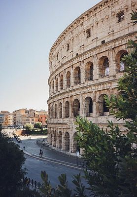 Colosseum in Rome beside a curved street, with buildings and trees under a clear sky
