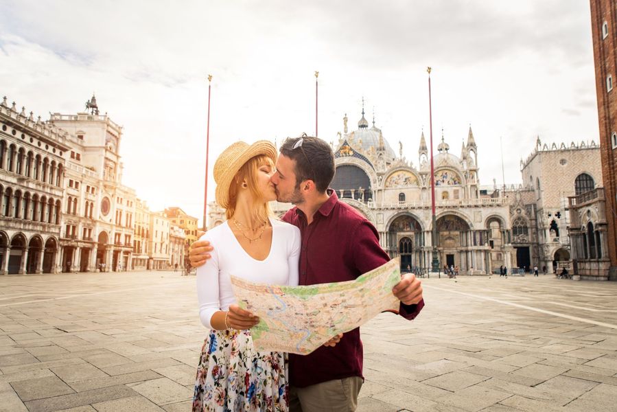 Couple kissing while holding a map in St. Mark’s Square, Venice, with a cathedral in the background