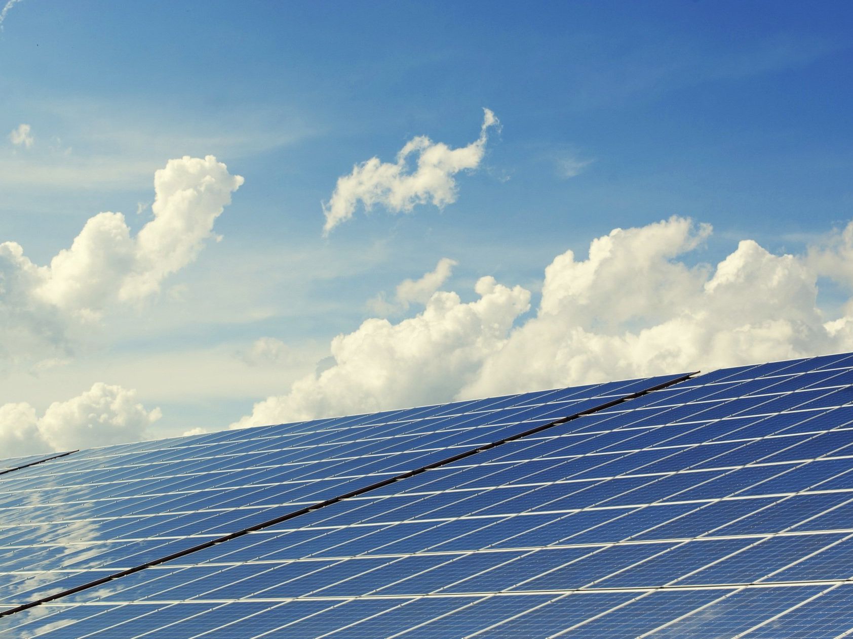A row of solar panels against a blue sky with clouds