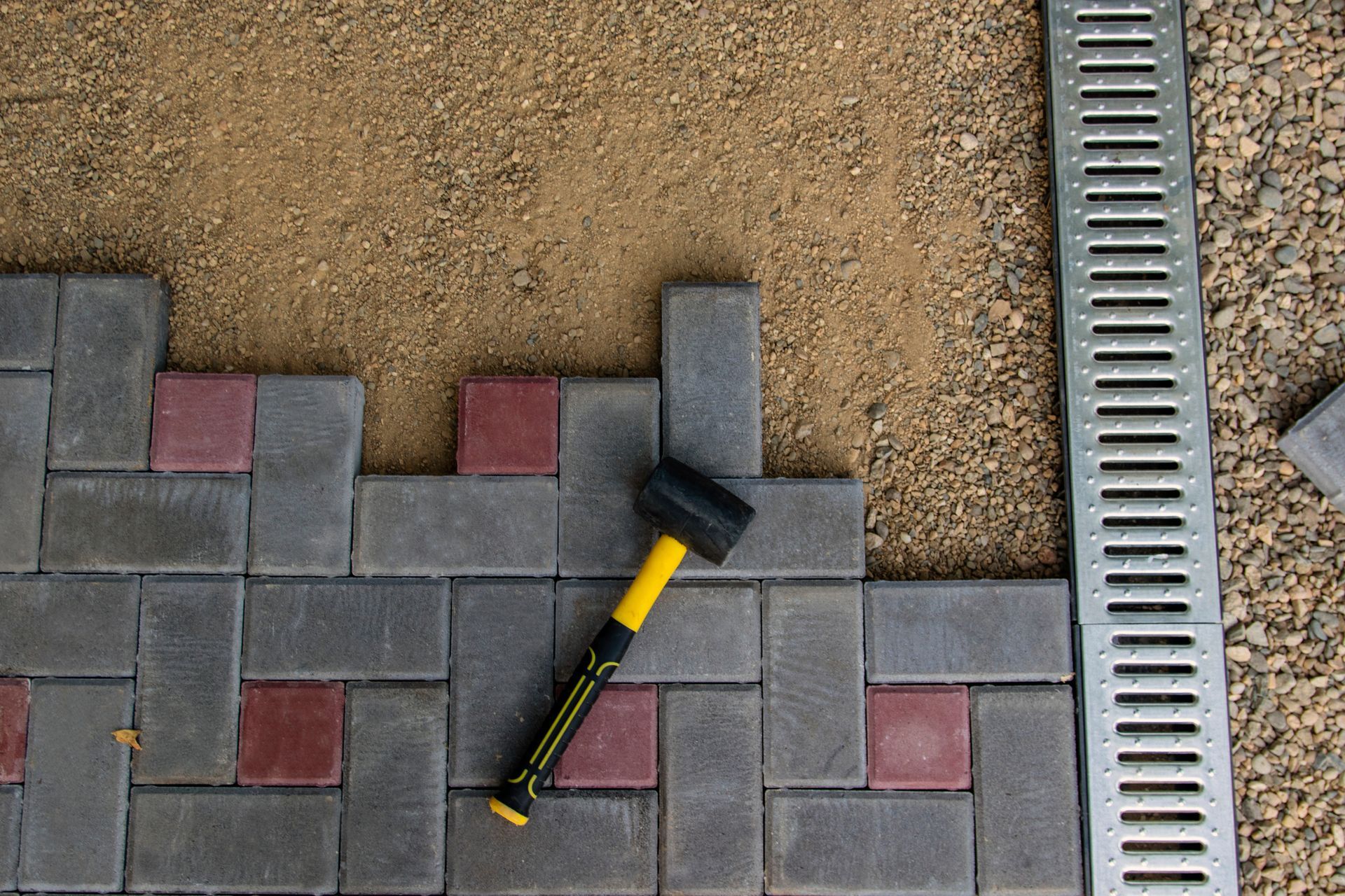 A yellow and black hammer is laying on a brick walkway.