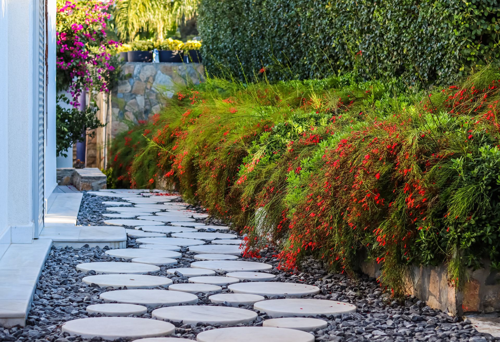 A stone walkway leading to a house surrounded by flowers and bushes.