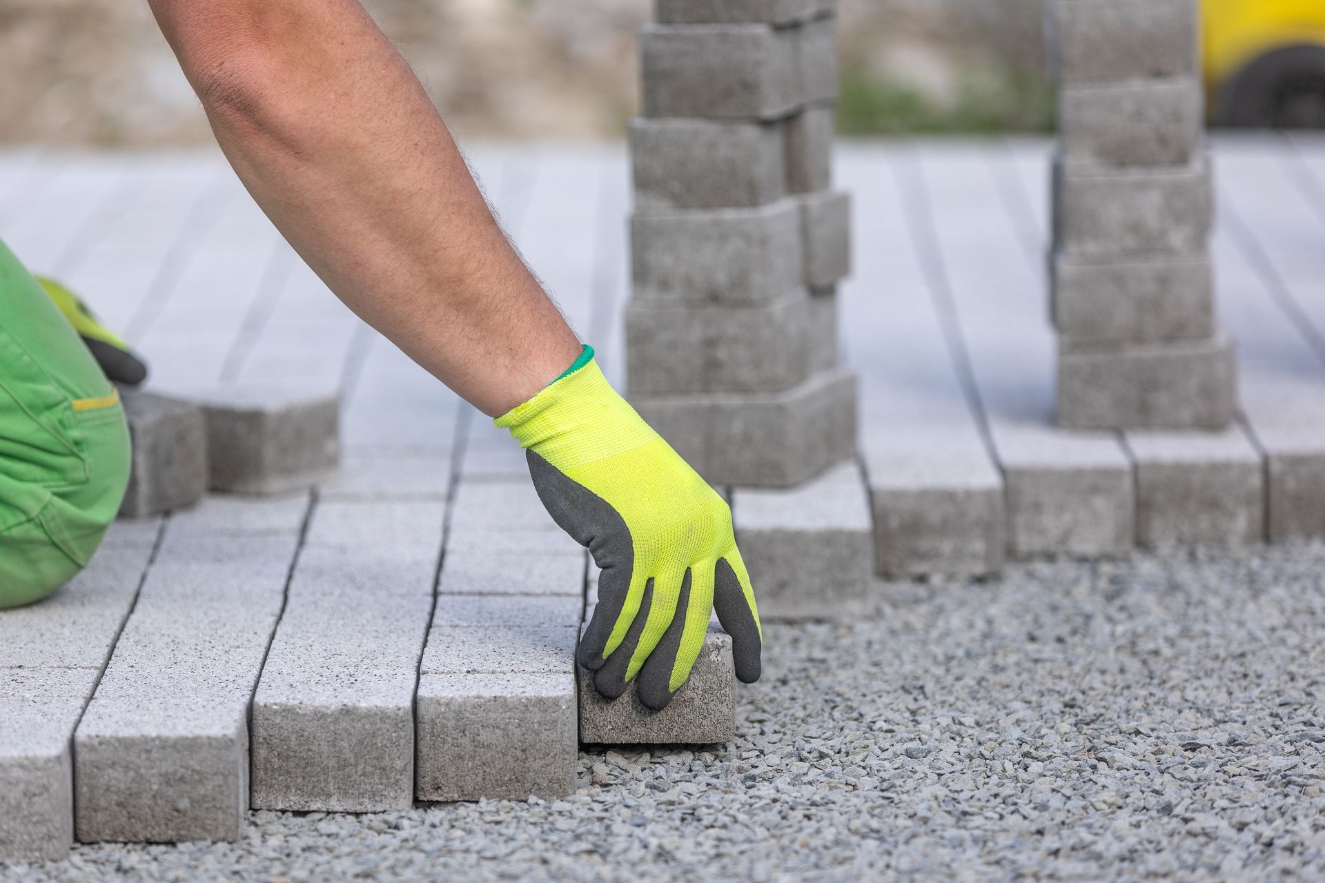 A man wearing yellow gloves is laying bricks on the ground.