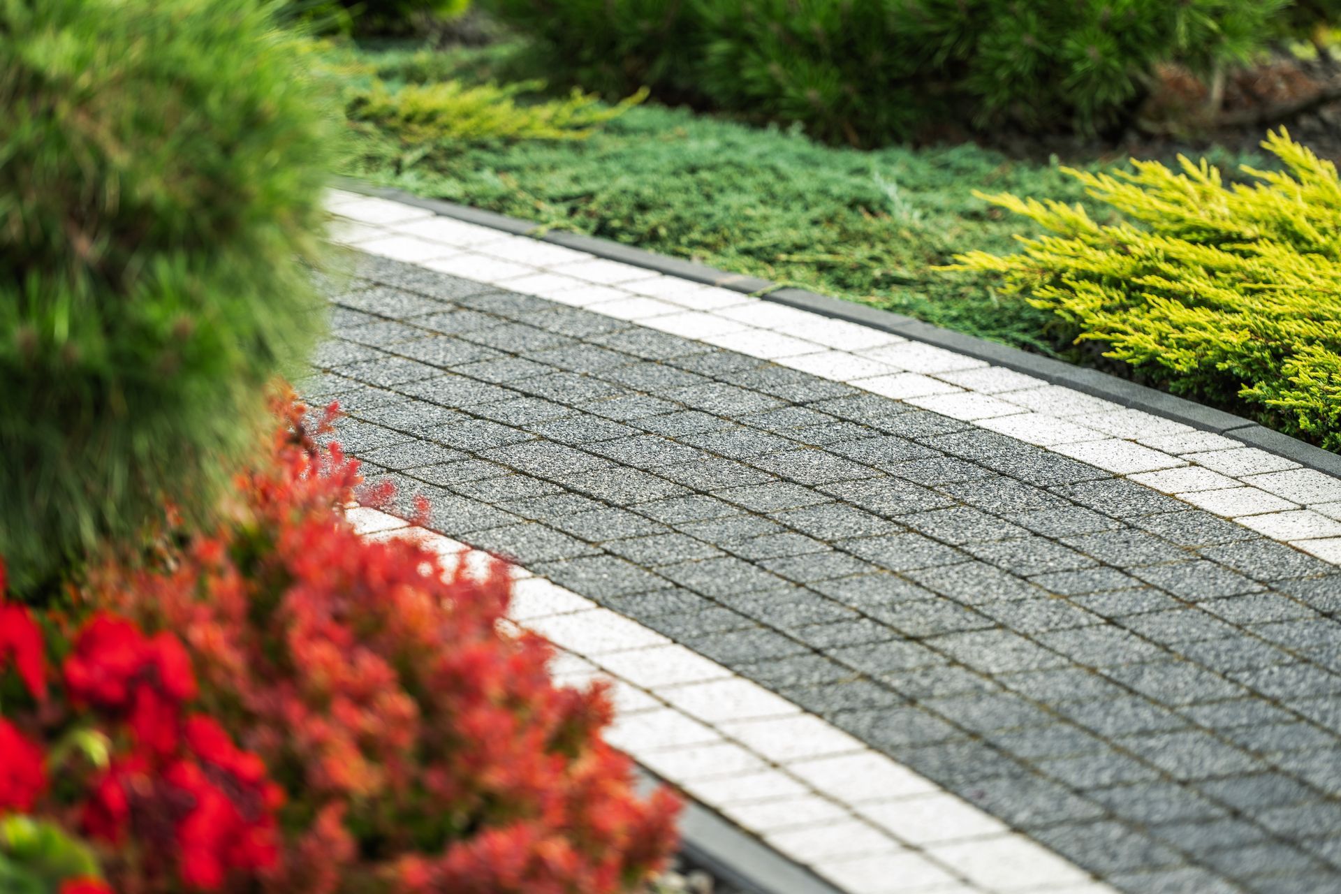 A brick walkway surrounded by flowers and trees in a garden.