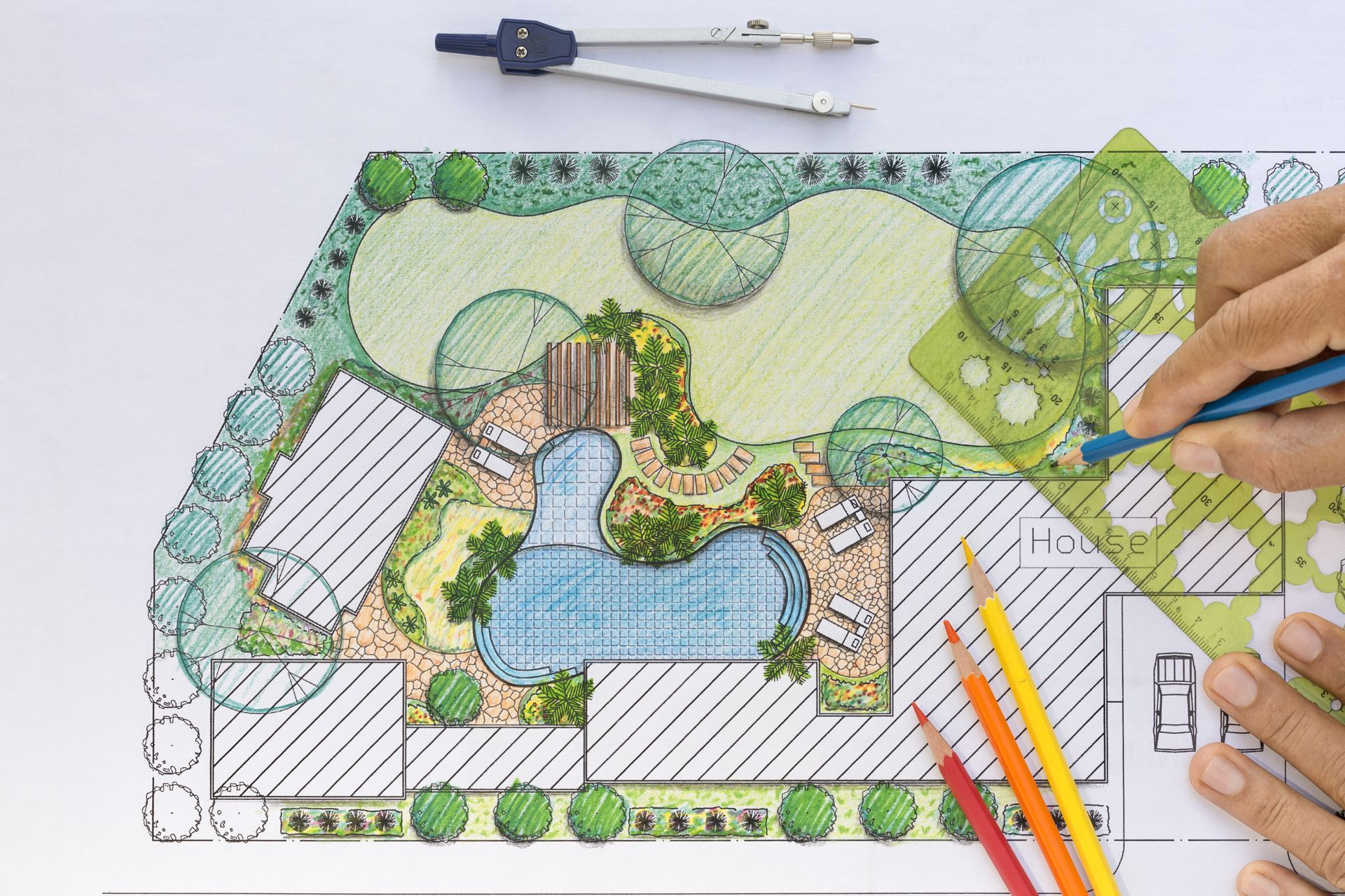 A person is drawing a garden plan with a compass and pencils.