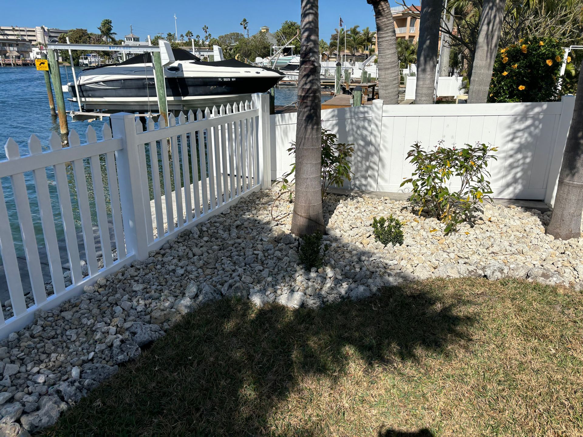 a white picket fence surrounds a yard with a boat in the background .
