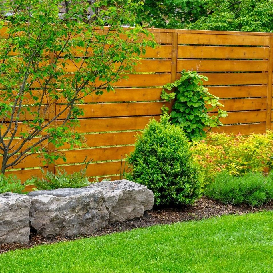 a wooden fence surrounds a lush green lawn in a backyard .