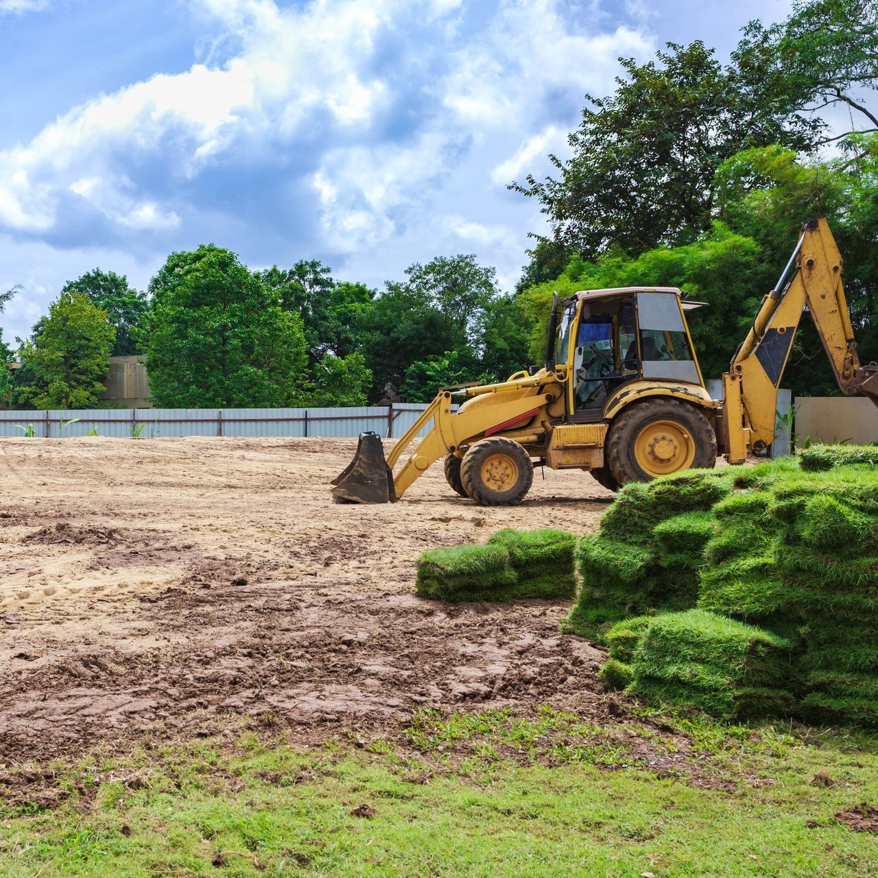 a yellow bulldozer is moving dirt in a field next to a pile of grass .