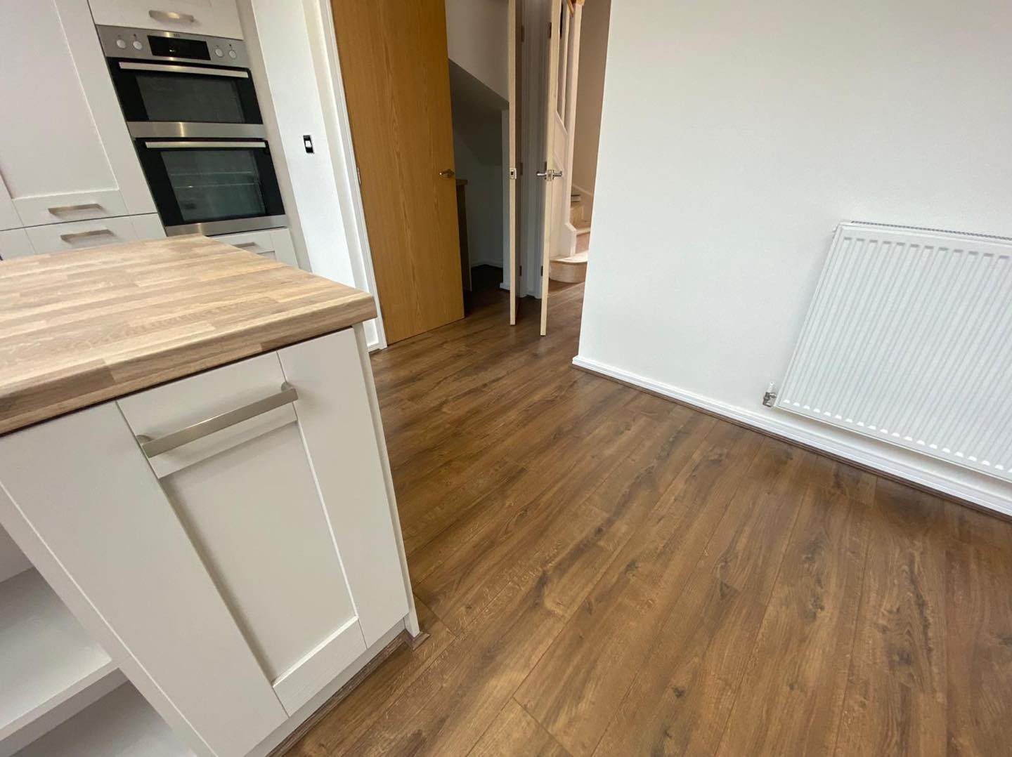 A kitchen with wooden floors , white cabinets , and a wooden counter top.
