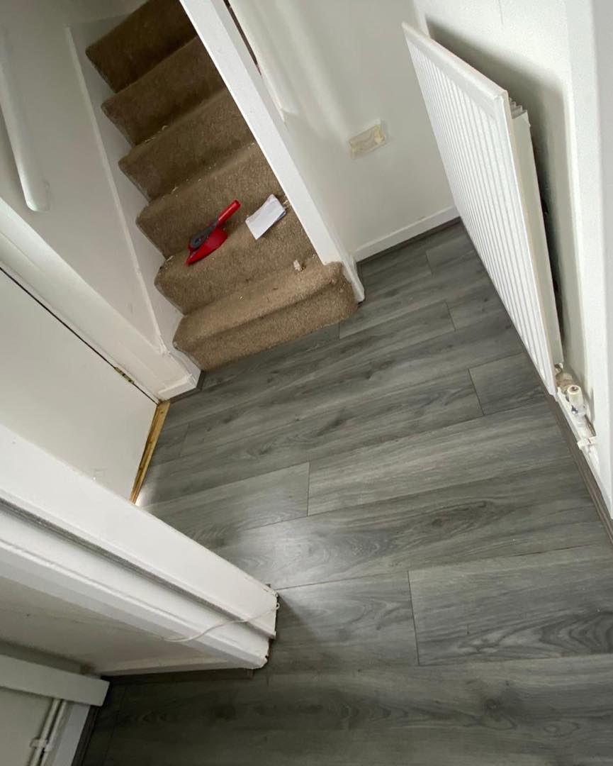 A hallway with stairs and a wooden floor.