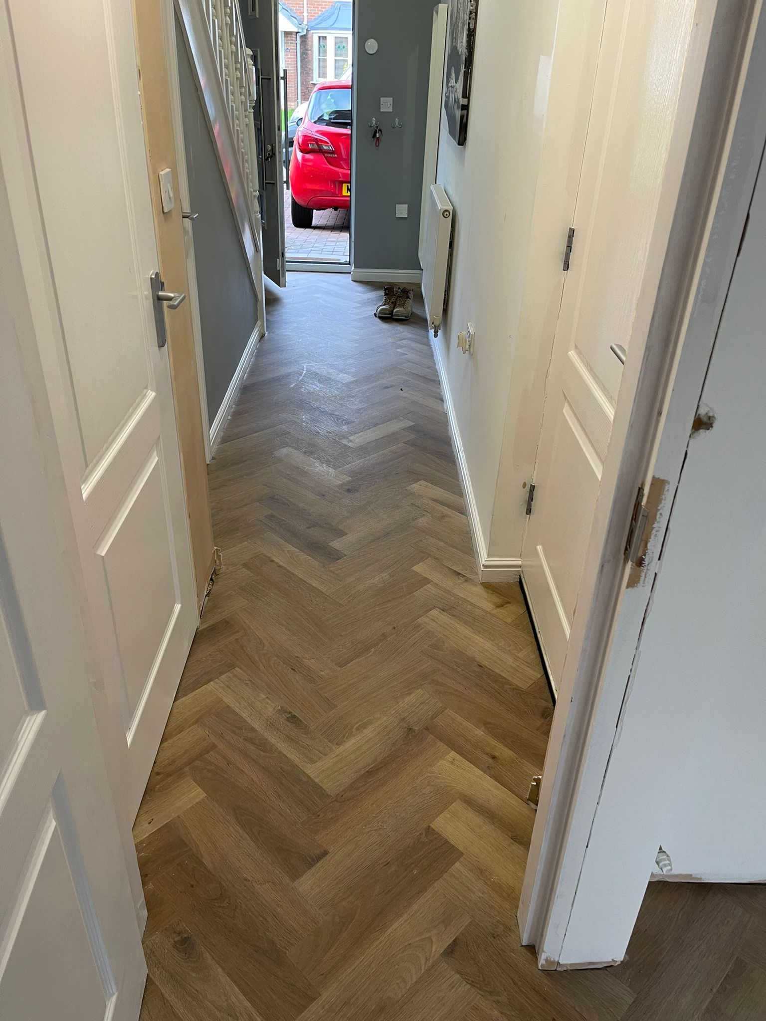 A hallway with a herringbone floor and a red car in the background.