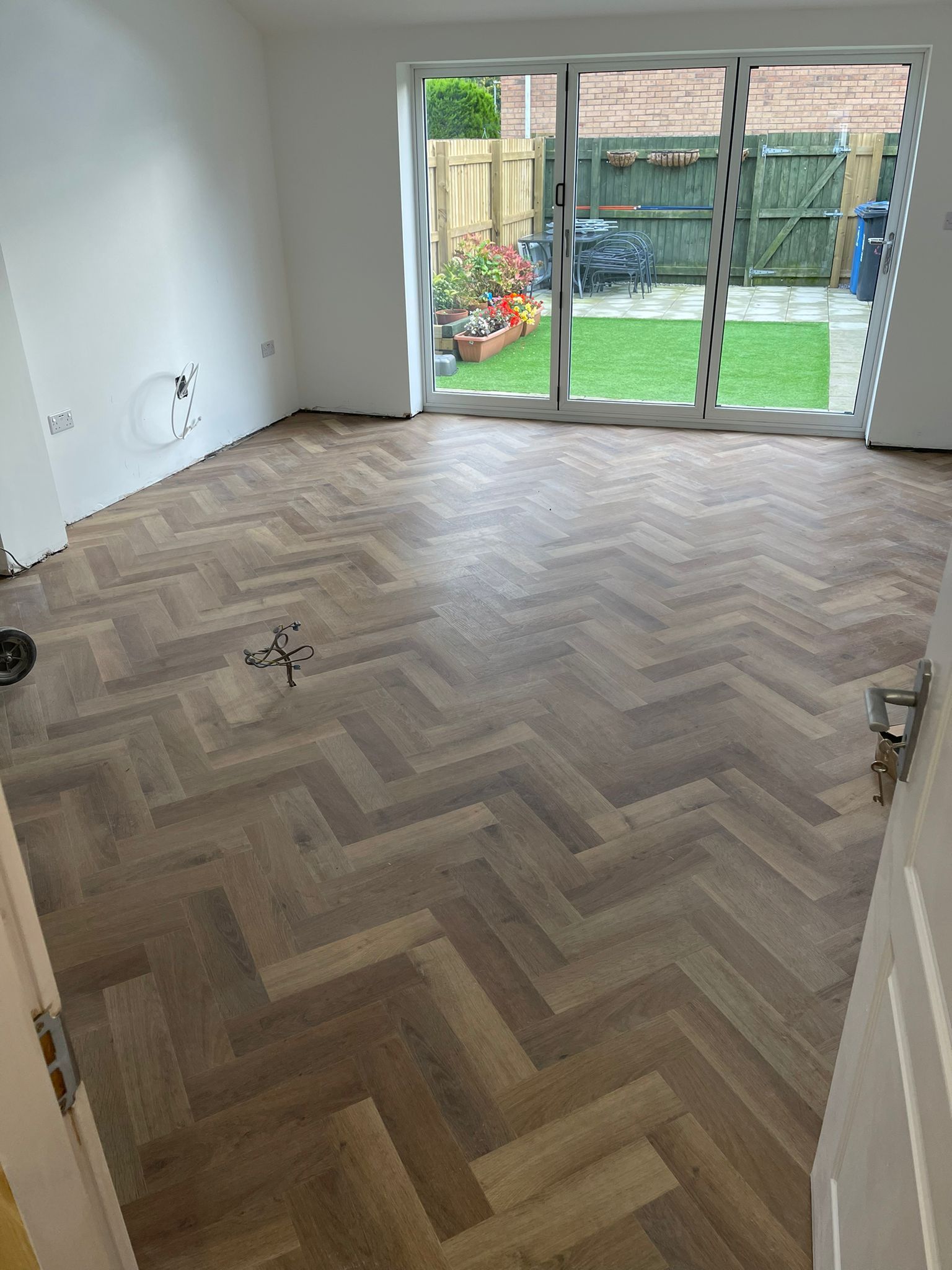 A living room with a herringbone floor and a sliding glass door.