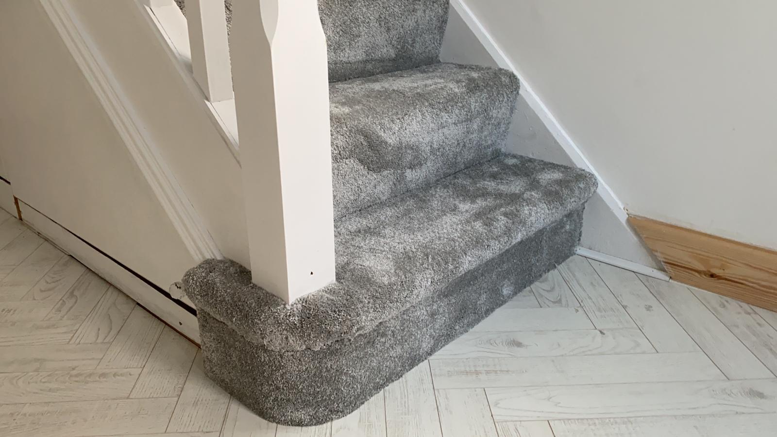 A close up of a staircase with a gray carpet and a white railing.