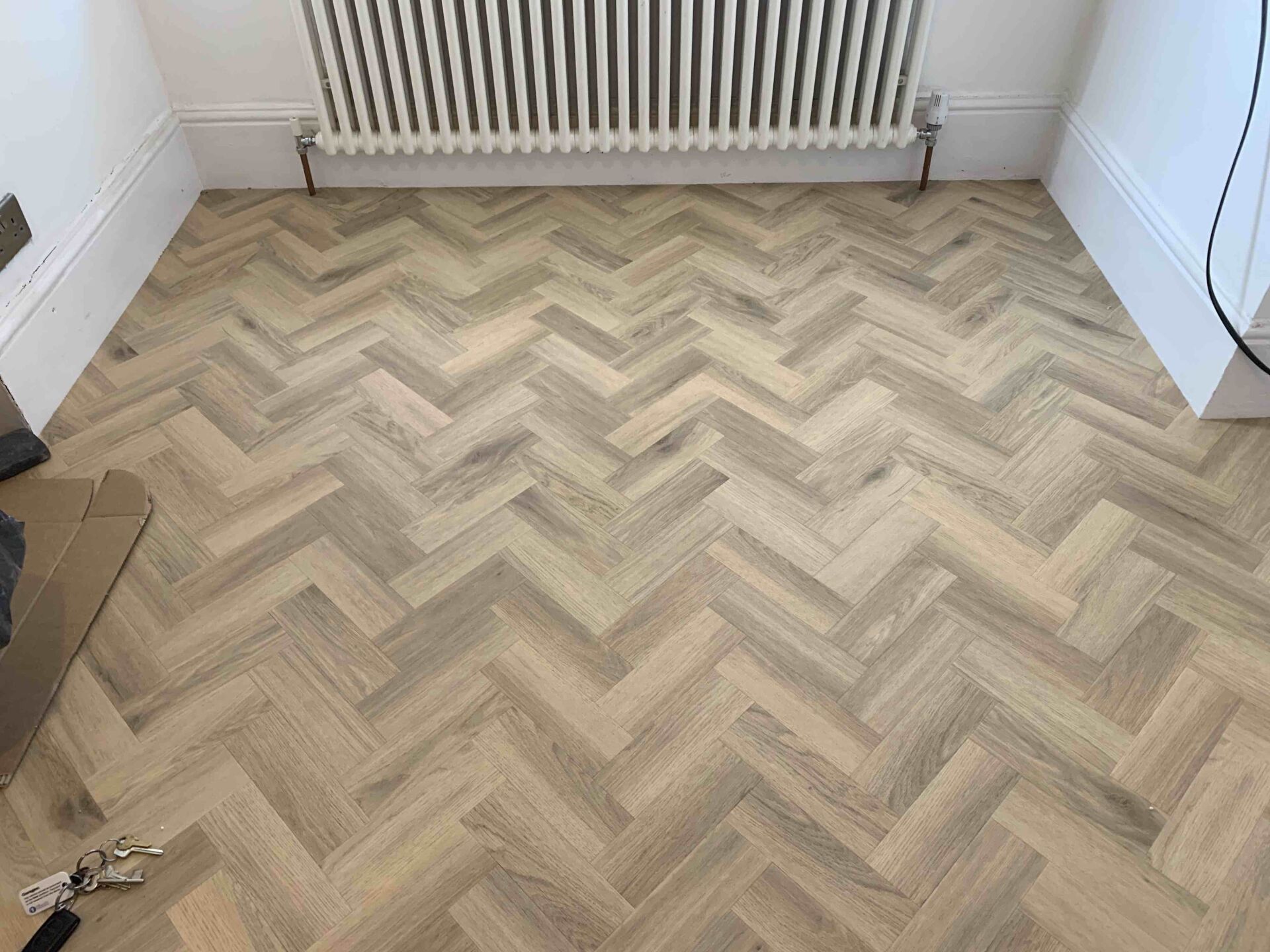 A room with a herringbone floor and a radiator.