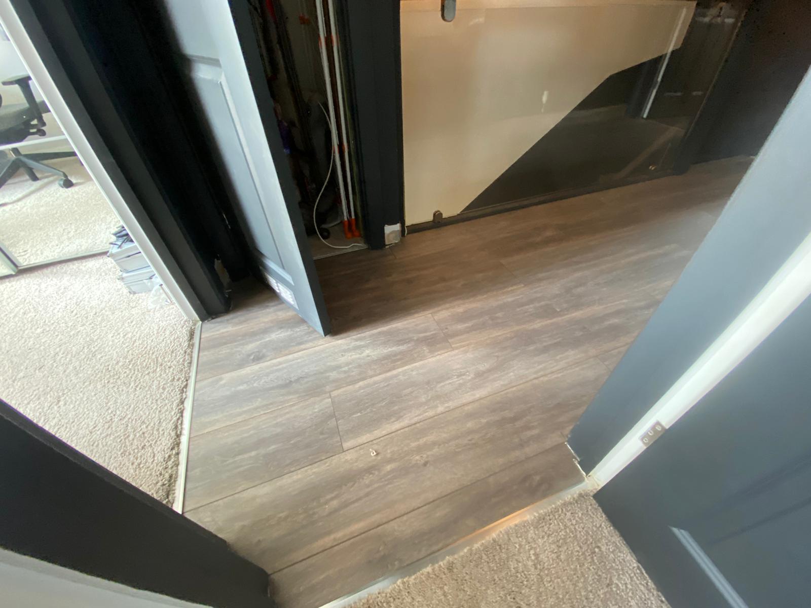 A doorway with a wooden floor and a staircase in the background.