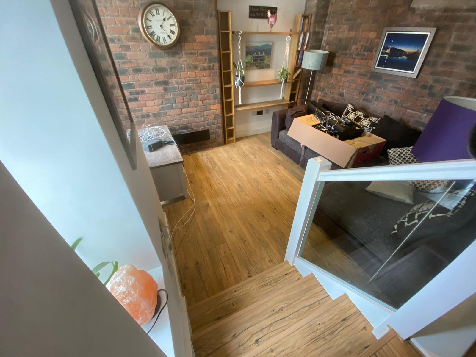A living room with a clock on the wall and stairs leading up to it.