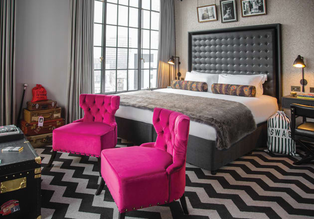 A bedroom with a king size bed and two pink chairs