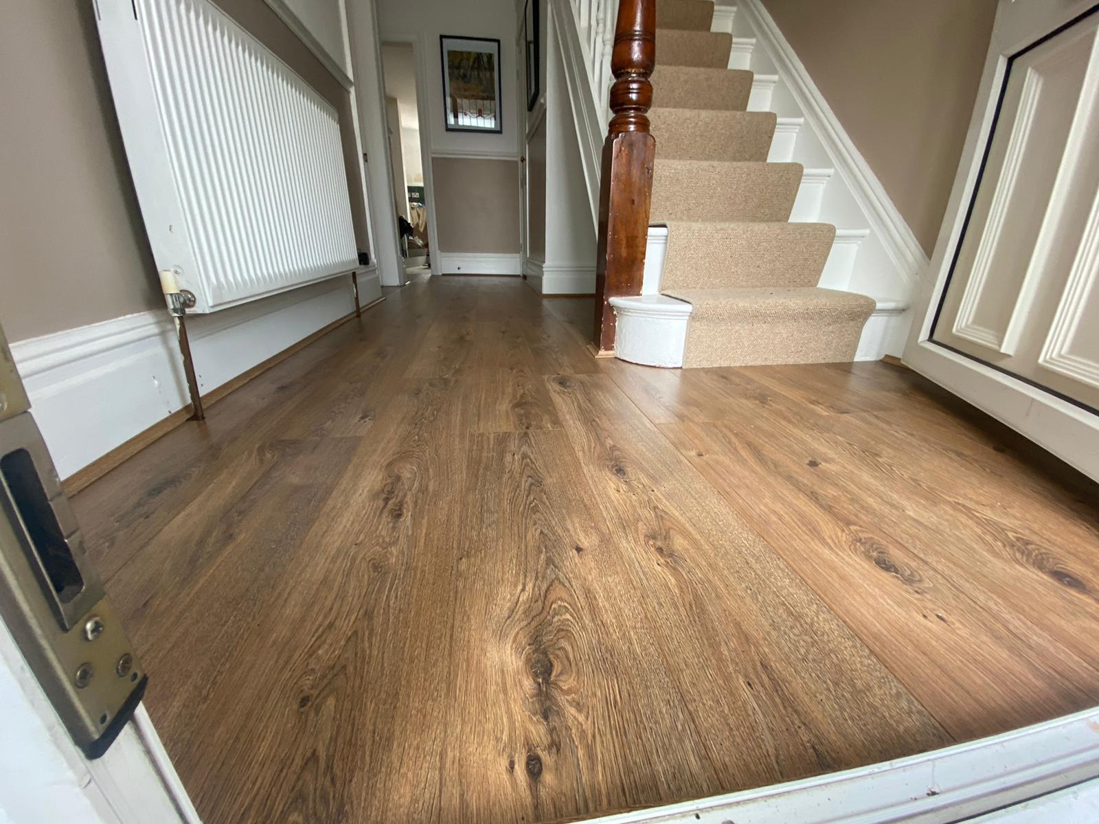 A hallway with wooden floors and stairs in a house.