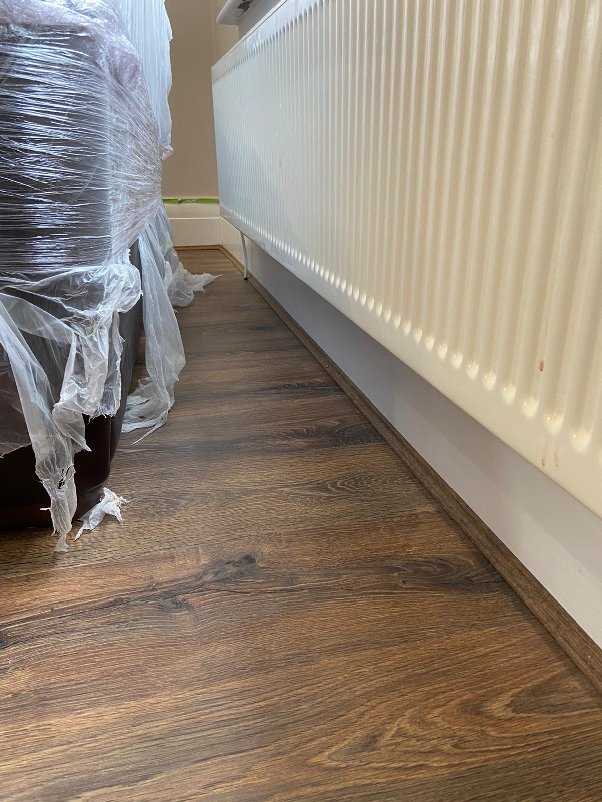 A couch wrapped in plastic is sitting next to a radiator on a wooden floor.
