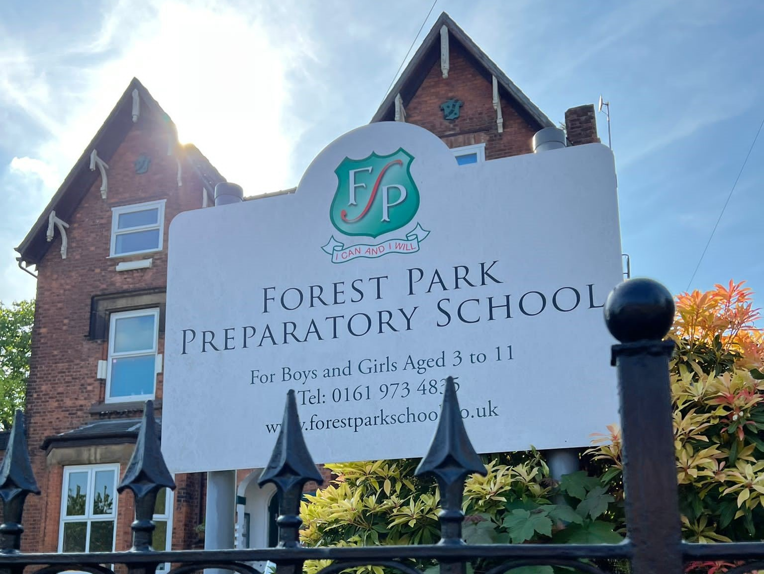 A sign for forest park preparatory school is behind a fence