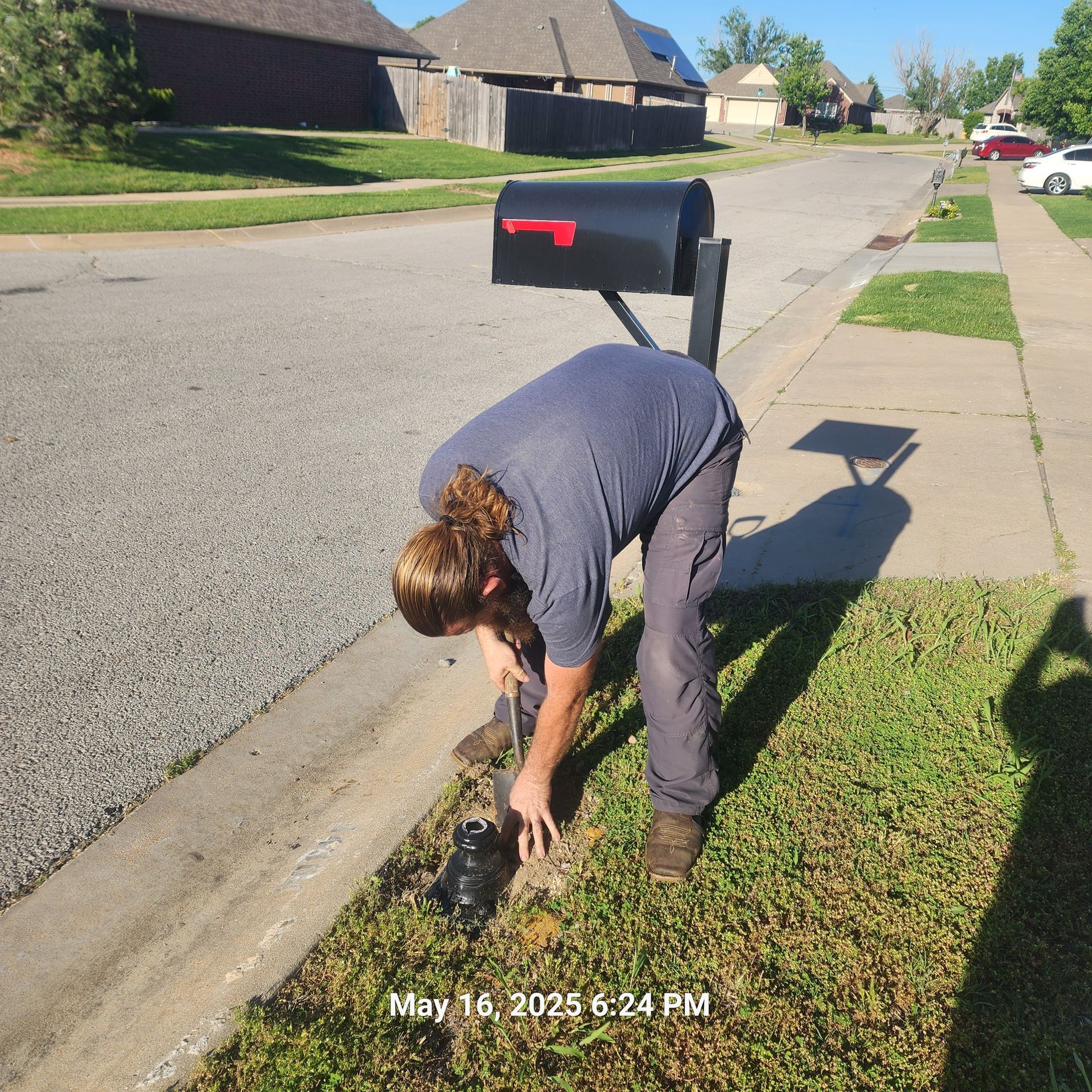 A man is kneeling next to a mailbox on the side of the road