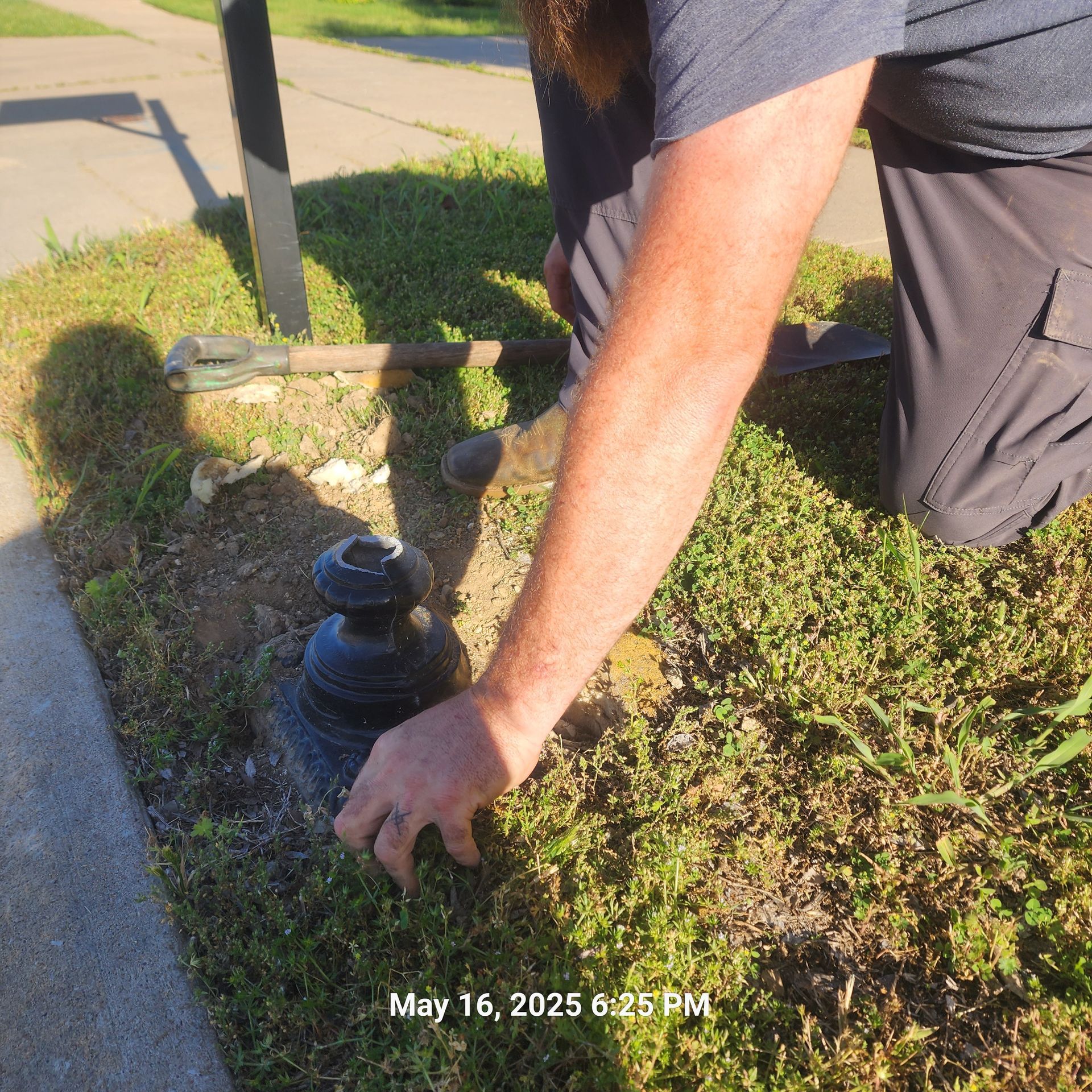 A man is kneeling down in the grass and working on a pole
