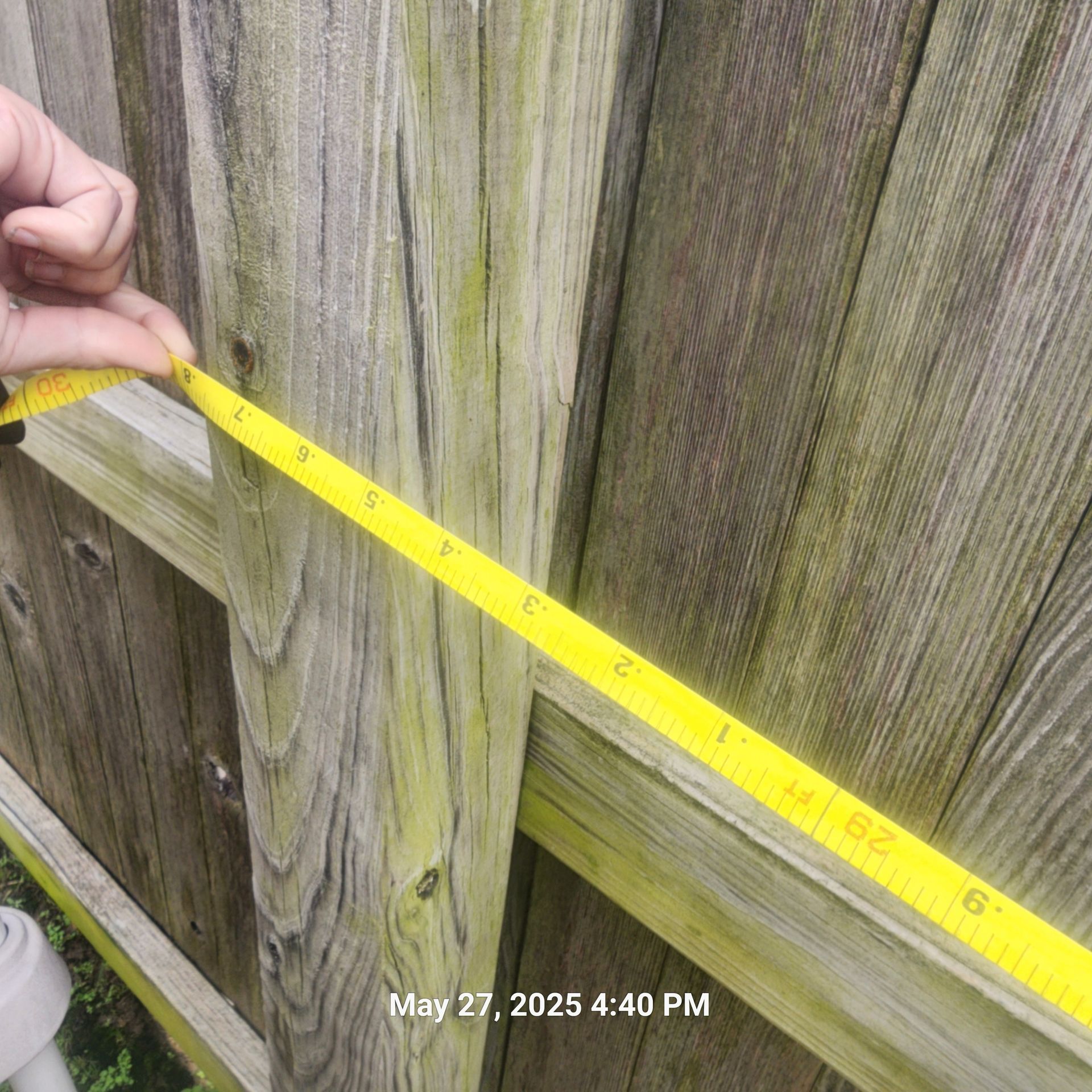 A person is measuring a wooden fence with a tape measure.