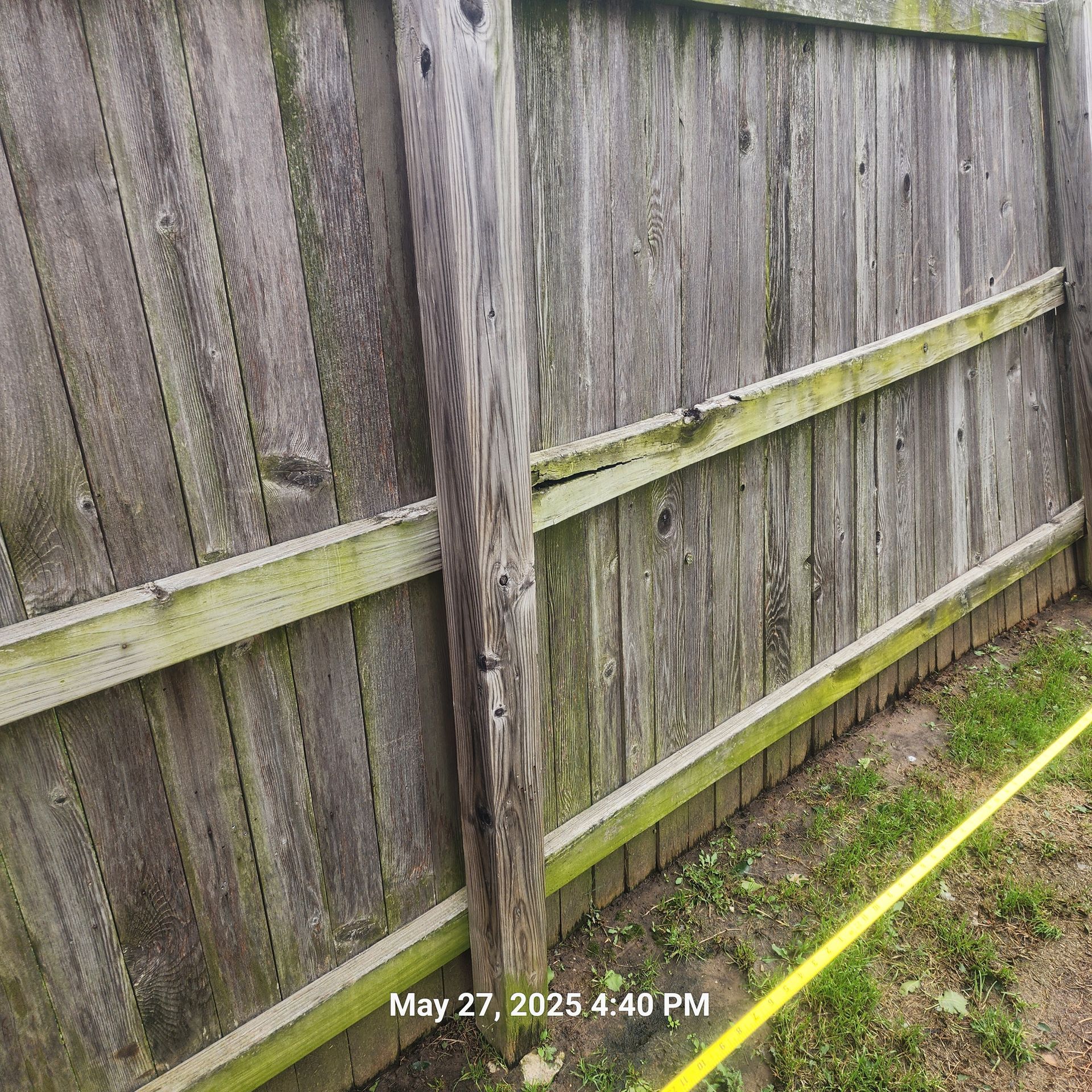 A wooden fence with a yellow hose next to it.