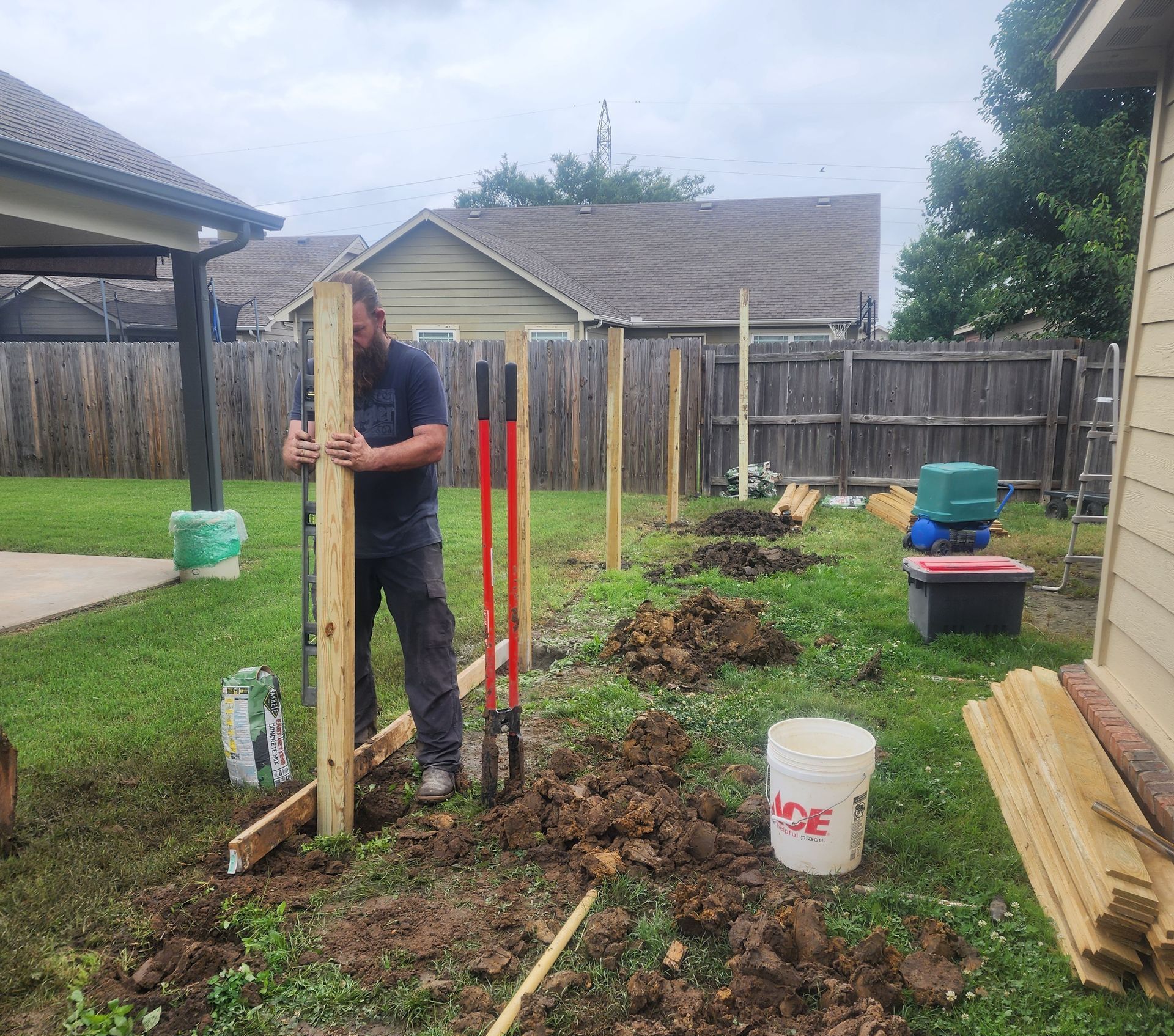 A man is standing in the dirt holding a wooden post.