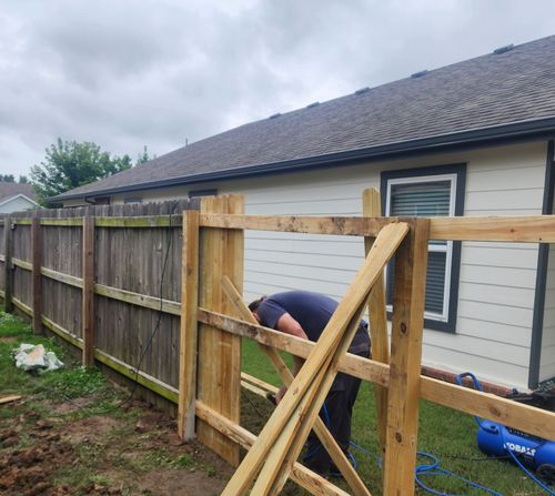 A man is working on a wooden fence in front of a house.