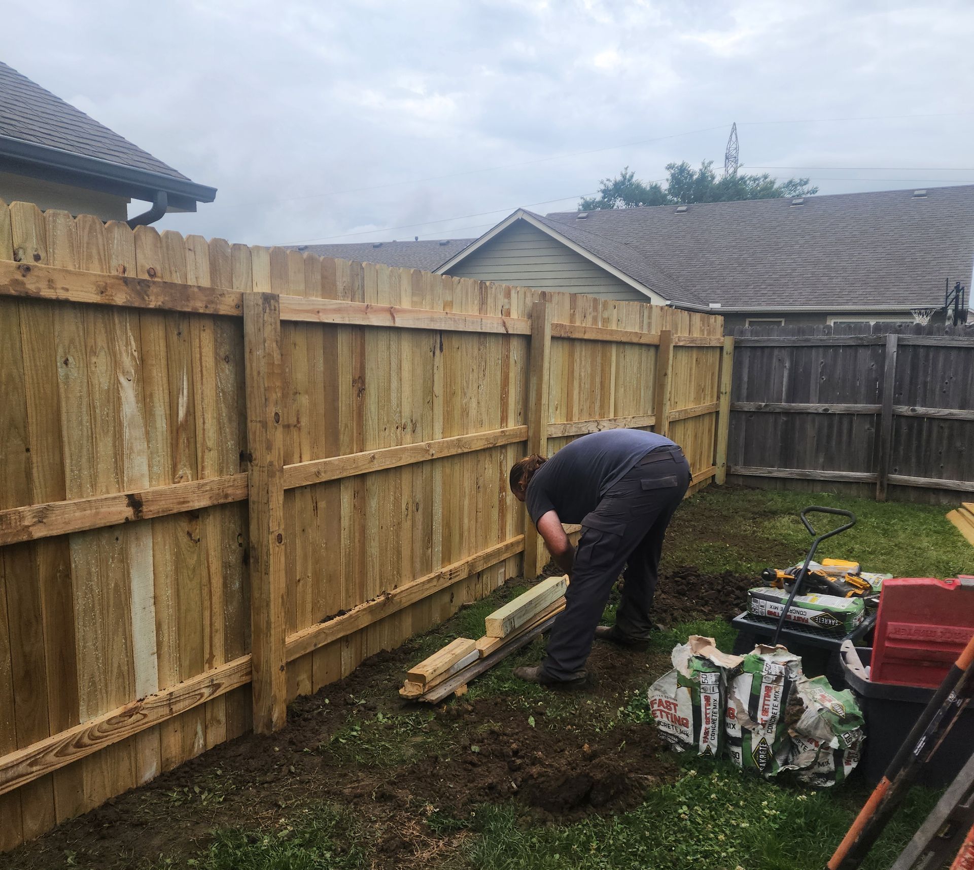 A man is working on a wooden fence in a backyard