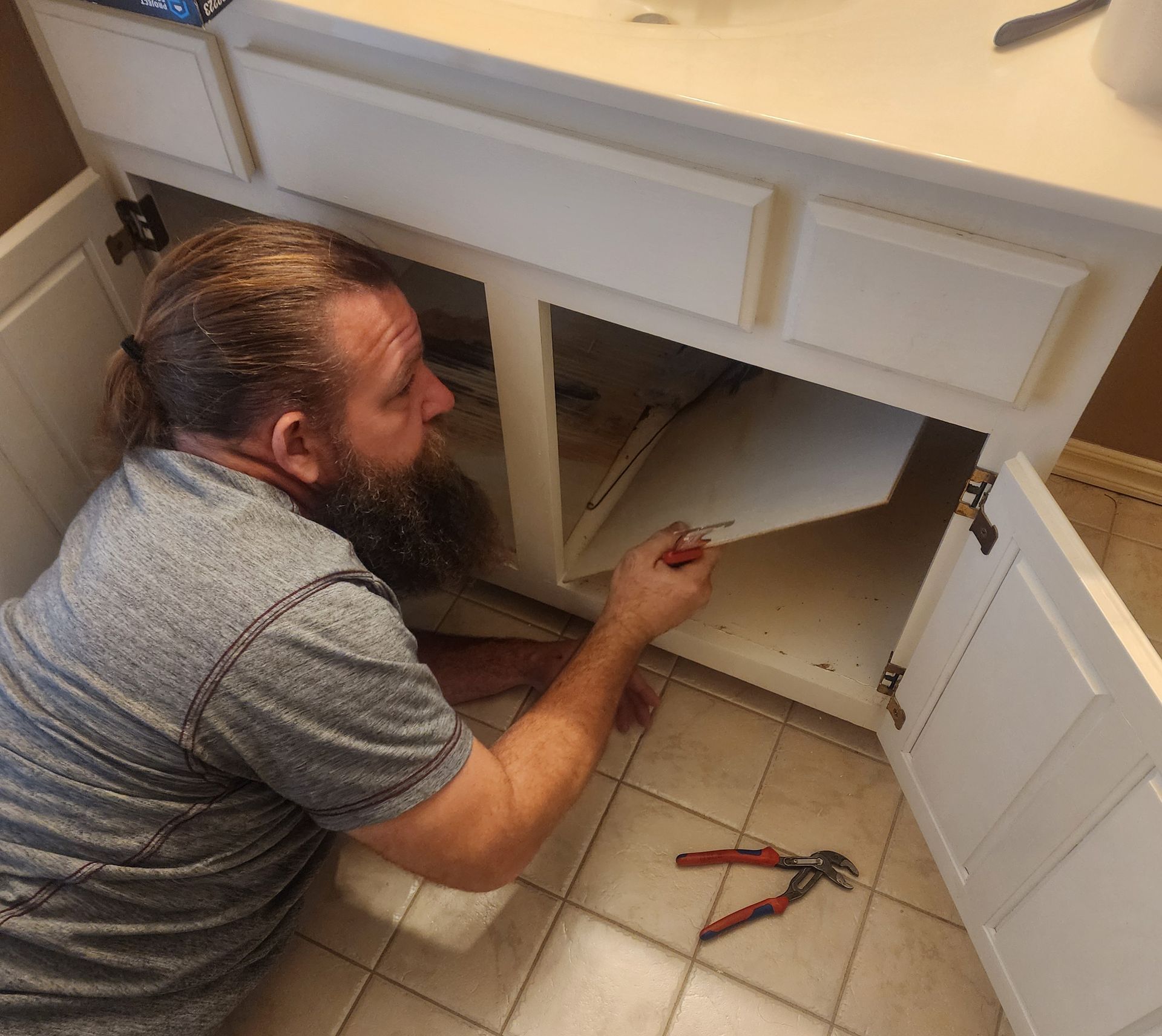 A man with a beard is working under a bathroom sink