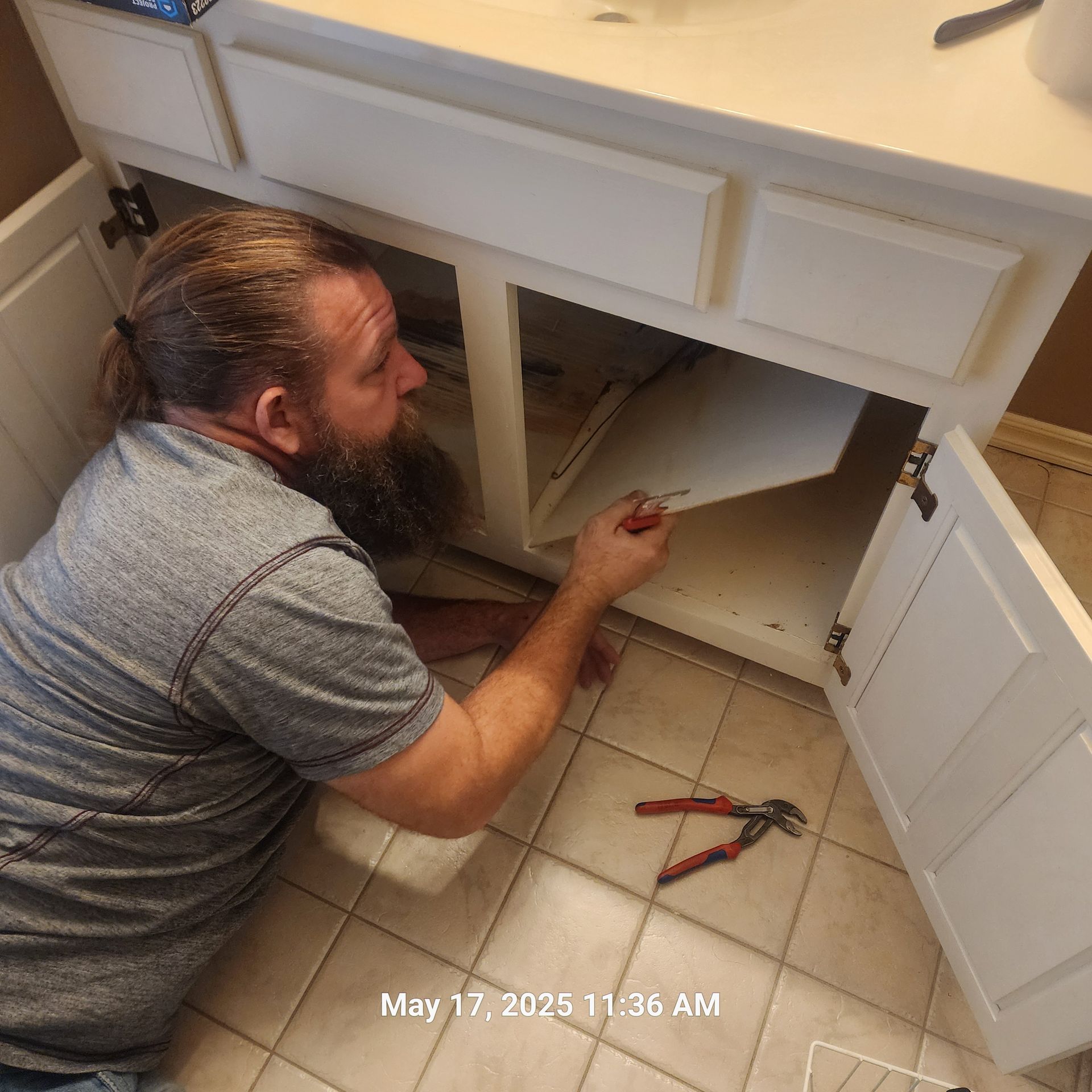 A man with a beard is working under a bathroom sink
