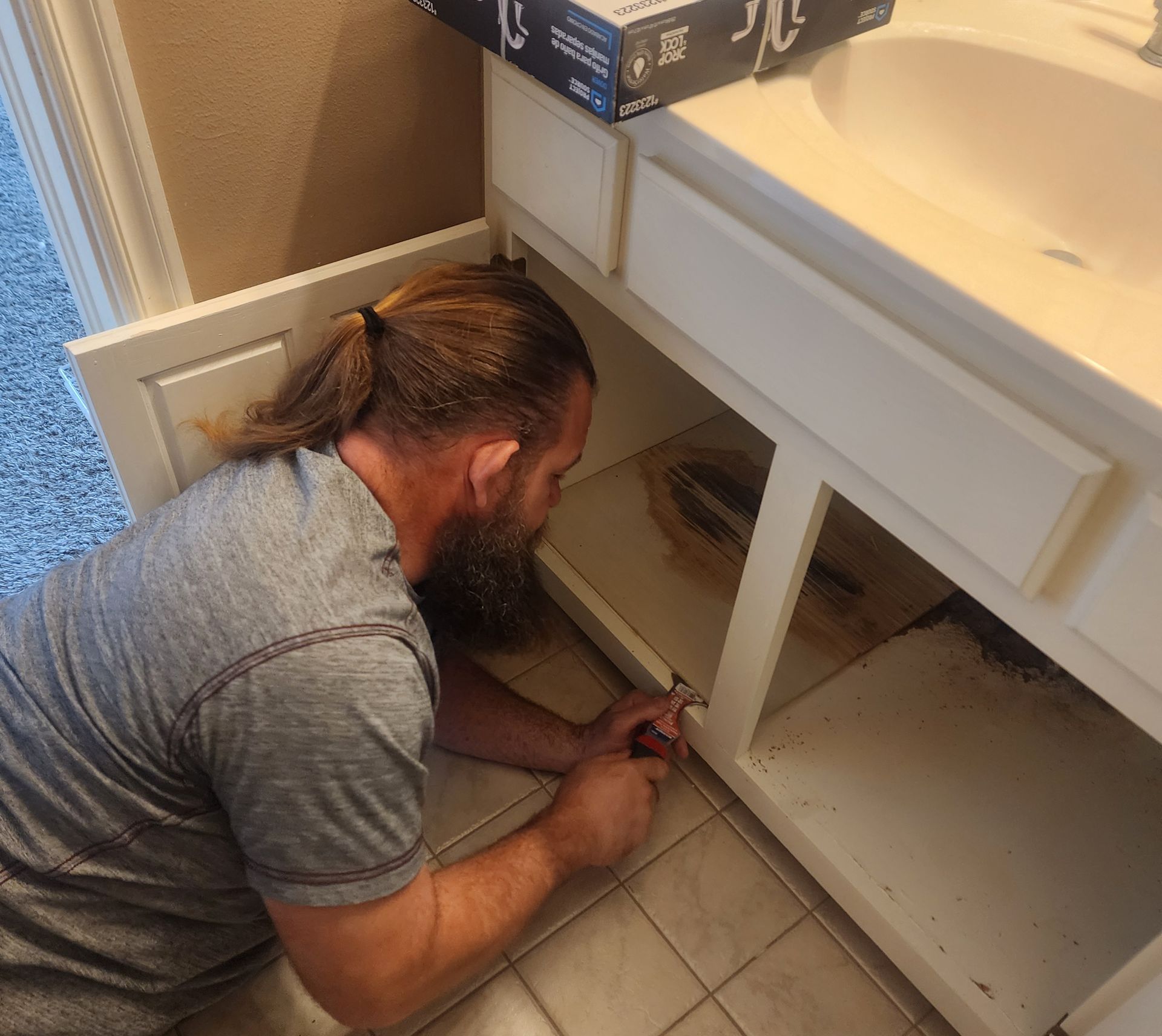 A man with a beard is working under a bathroom sink