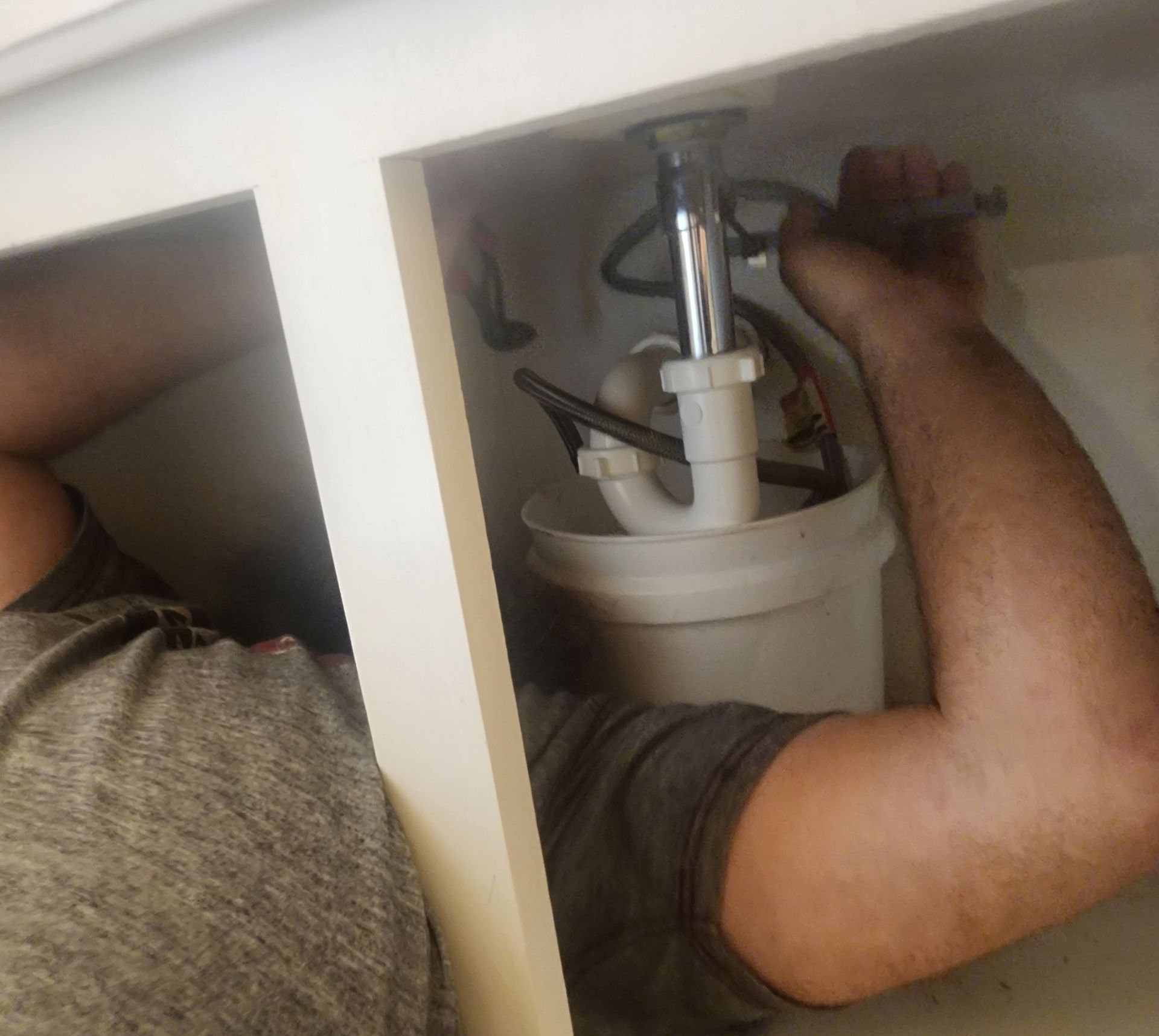 A man is fixing a sink with a wrench.