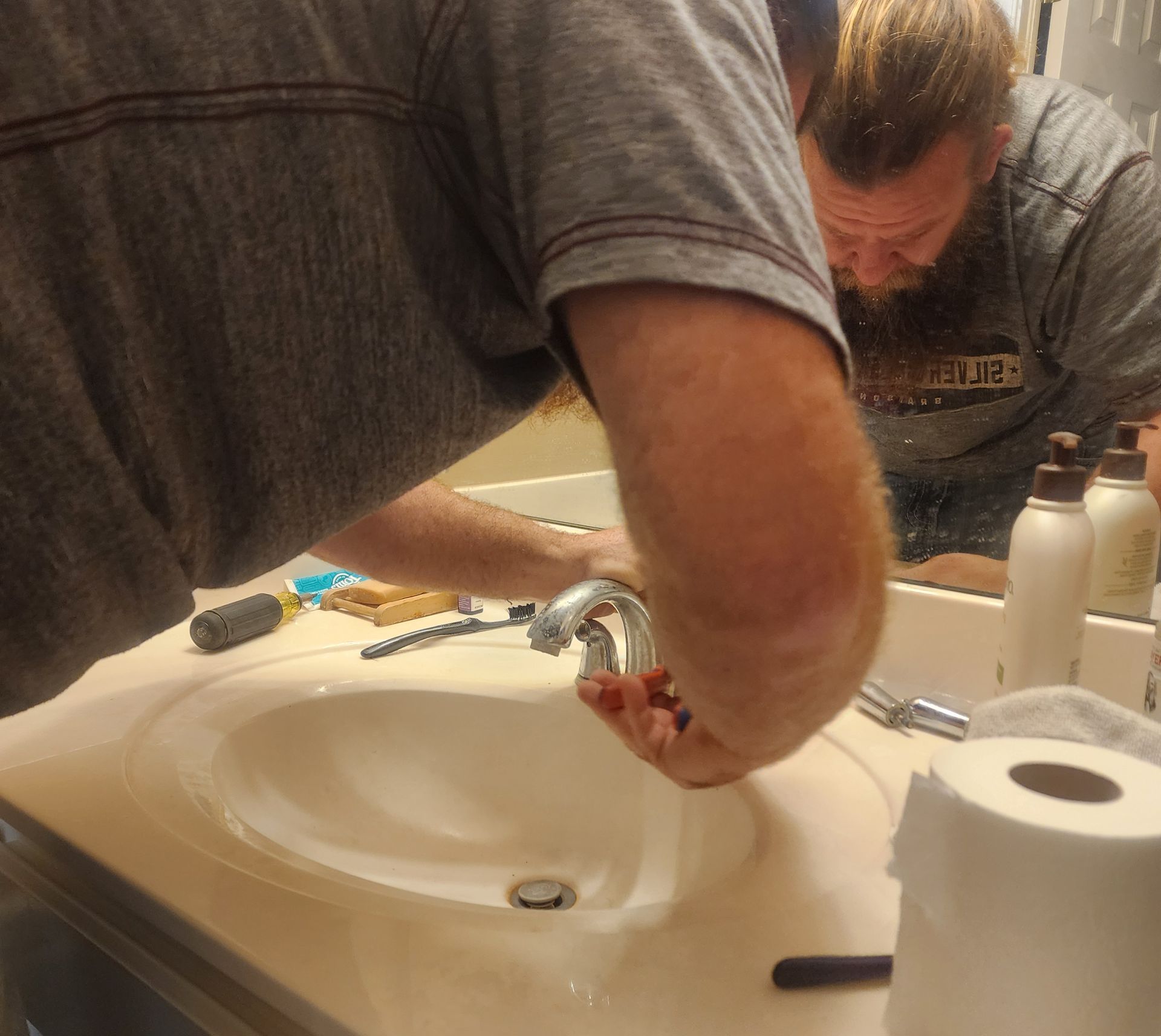 A man is fixing a faucet in a bathroom sink