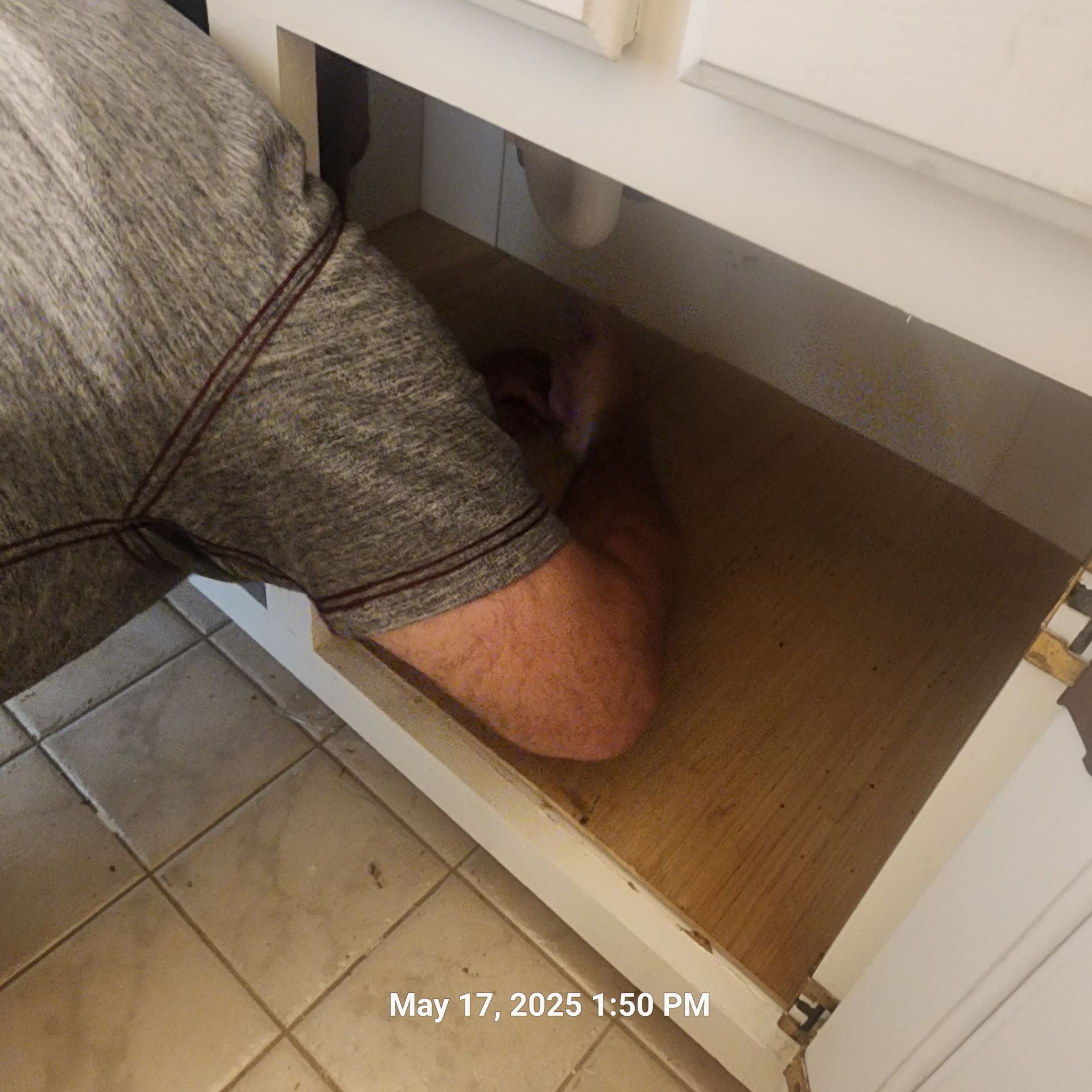 A man is kneeling under a sink on may 17th at 1:50 pm
