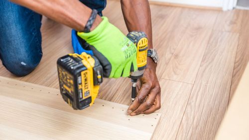A man is using a drill on a wooden floor.