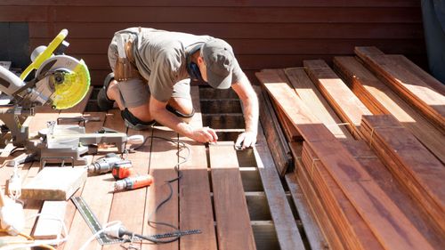 A man is working on a wooden deck with a circular saw.