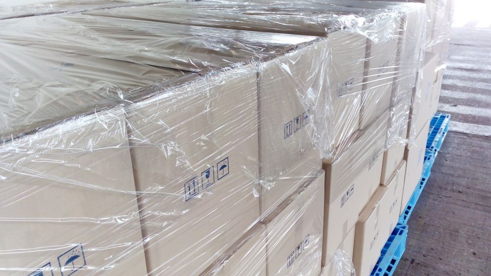 A Stack of Cardboard Boxes Wrapped in Plastic Sitting on Top of a Blue Pallet — Huskisson Self Storage in Vincentia, NSW