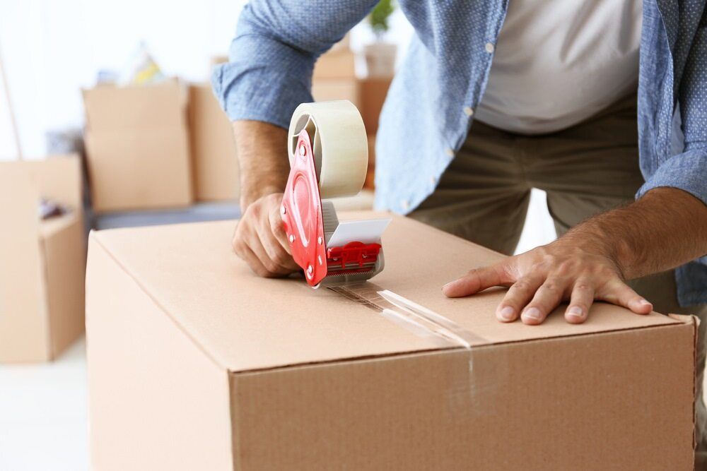 A Man is Taping a Cardboard Box With Tape — Huskisson Self Storage in Jervis Bay, NSW