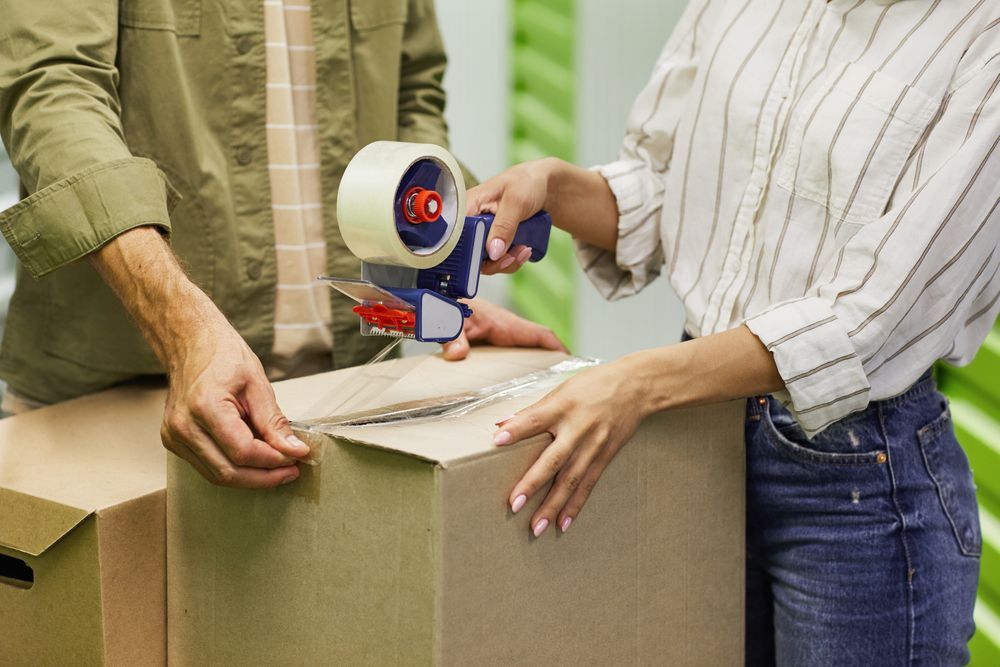 A Man and a Woman Are Wrapping a Cardboard Box With Tape — Huskisson Self Storage in Huskisson, NSW