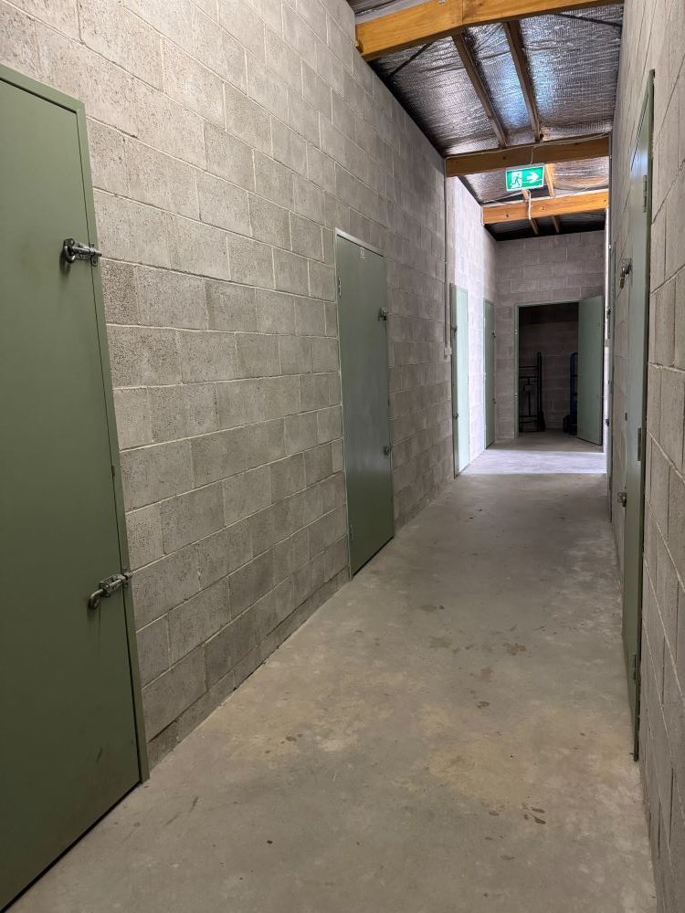 A Long Hallway With Brick Walls and Green Doors in a Building — Huskisson Self Storage in St Georges Basin, NSW