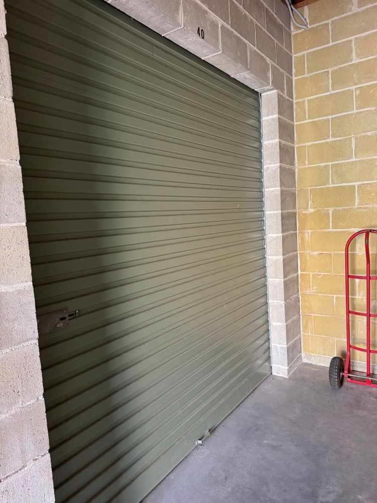 A Green Garage Door is in a Brick Building Next to a Red Dolly — Huskisson Self Storage in Jervis Bay, NSW