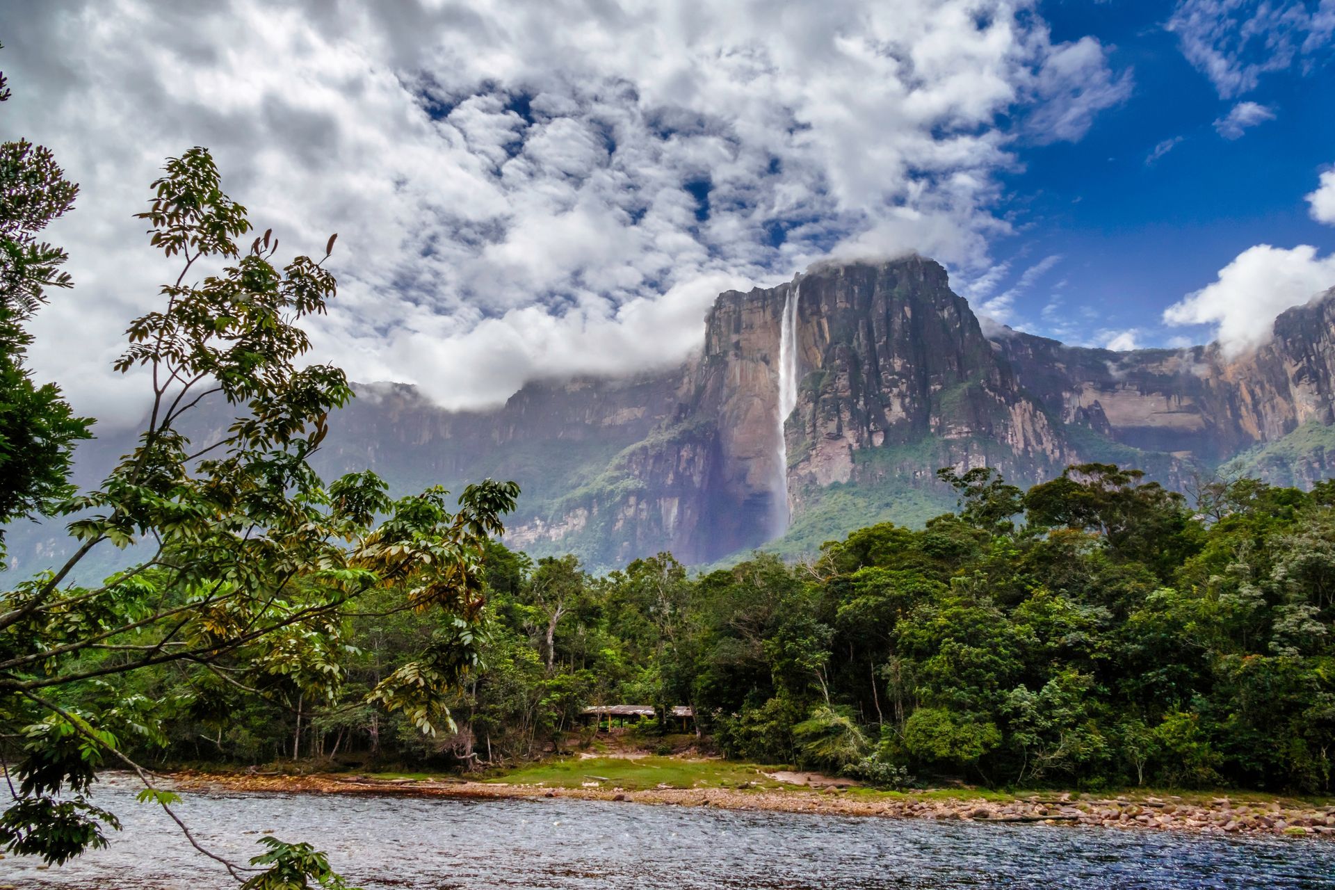 Angel Falls is in Canaima National Park, Venezuela, and water comes down next to a river surrounded by trees.