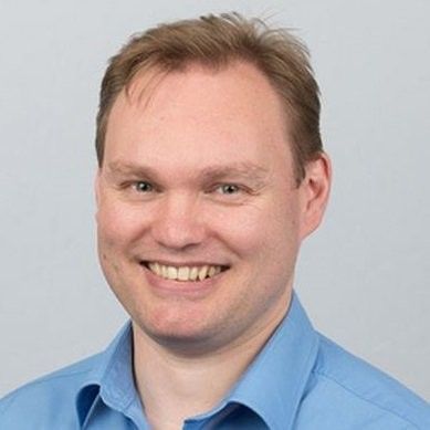 Smiling man in a blue shirt against a light gray background