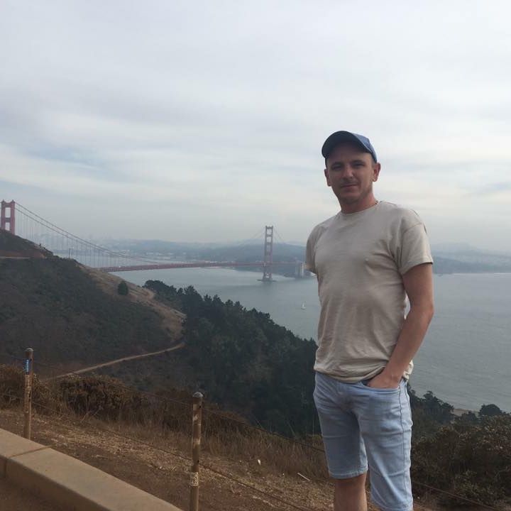 Man in cap and shorts poses with the Golden Gate Bridge in the background.